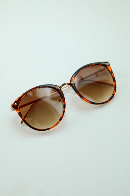 Sunglasses with tortoiseshell frame and gradient lenses on a light blue background