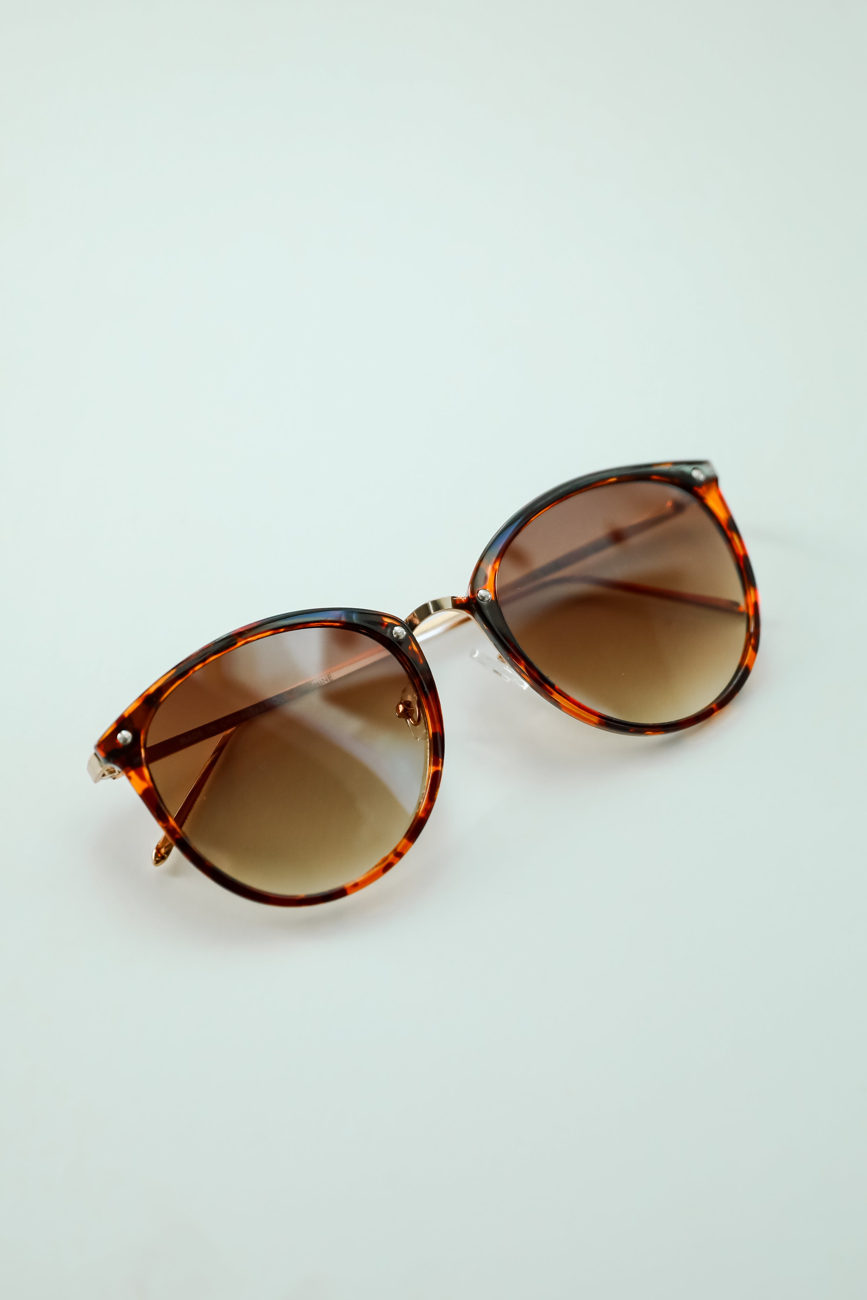 Sunglasses with tortoiseshell frame and brown lenses on a light gray background