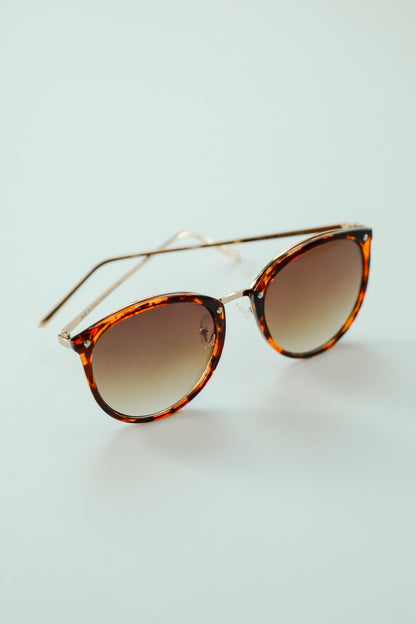 Tortoiseshell sunglasses with gold frames on a light blue background
