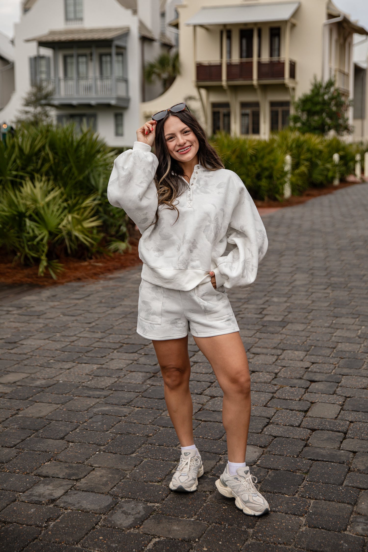Woman in a white outfit standing on a cobblestone street with houses in the background
