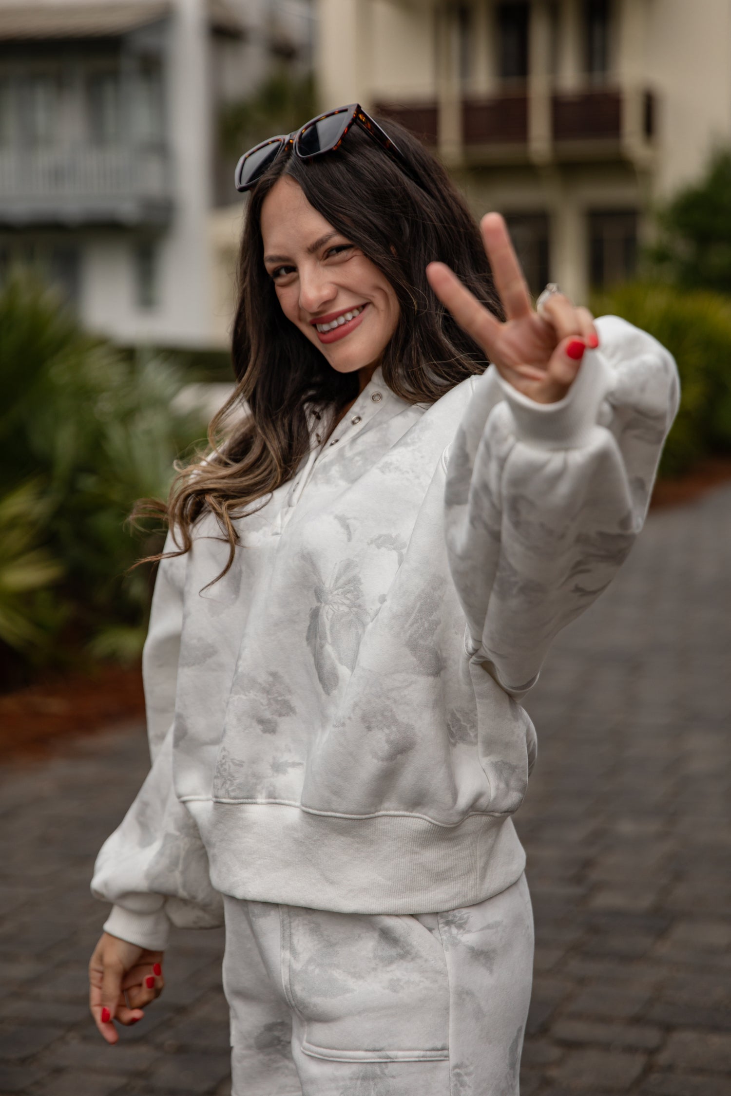 Woman in a gray tracksuit making a peace sign outdoors.