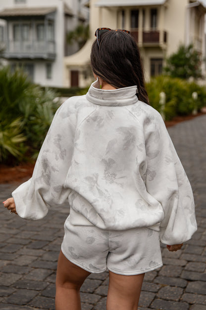 Person wearing a gray tie-dye outfit walking on a street.