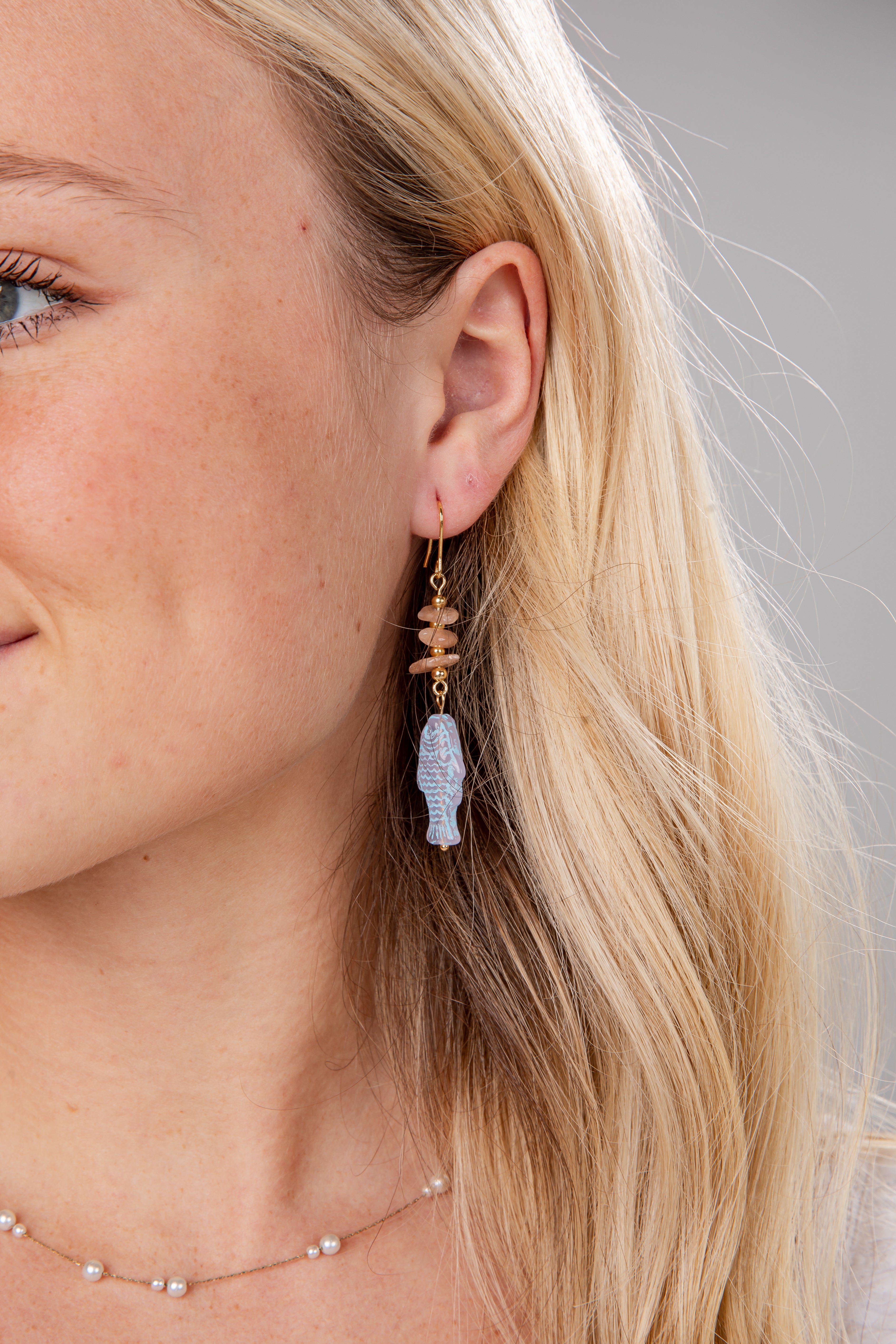 Close-up of a woman wearing a unique earring with a blue gemstone and gold accents.