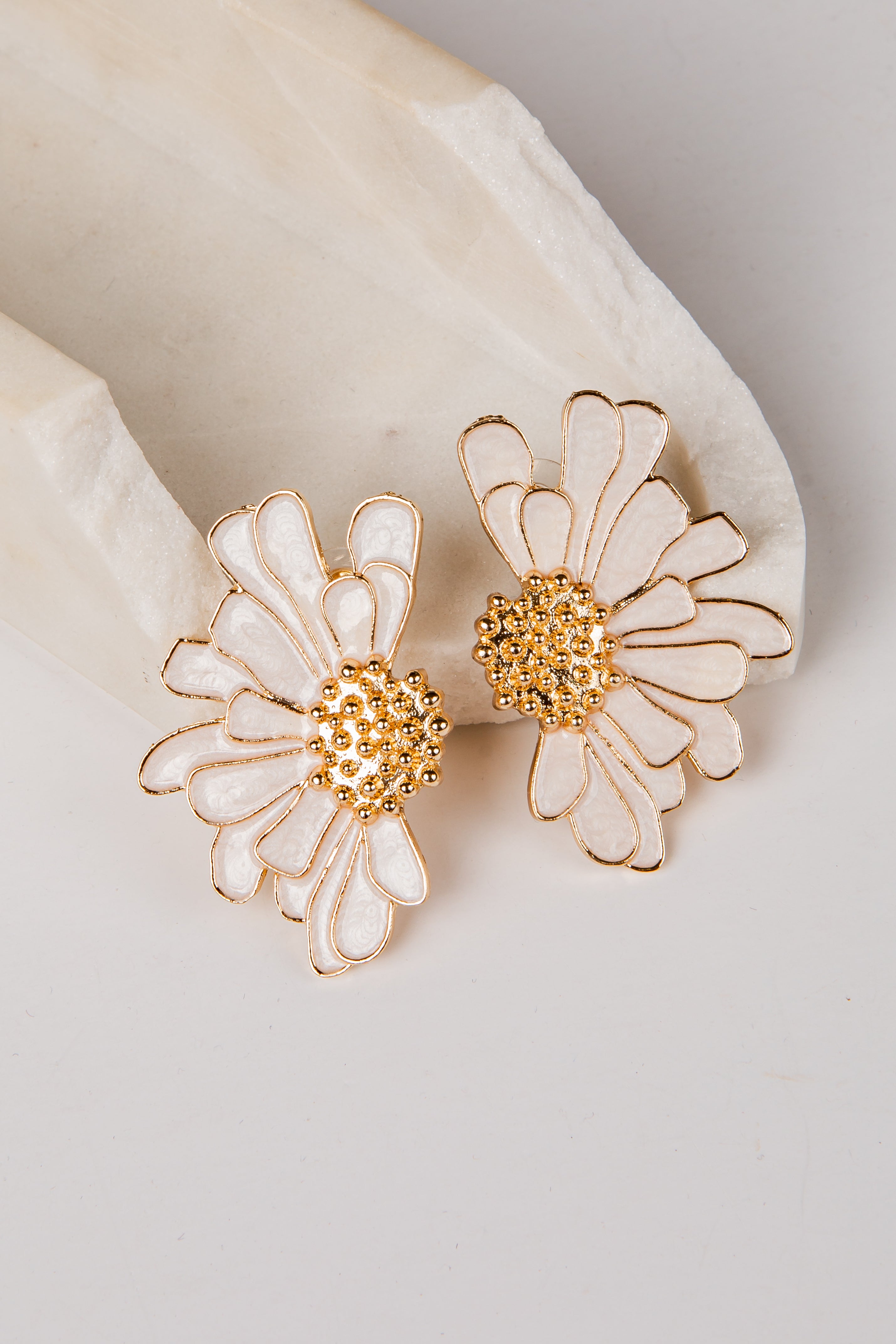Pair of flower-shaped earrings with gold and white details on a light background