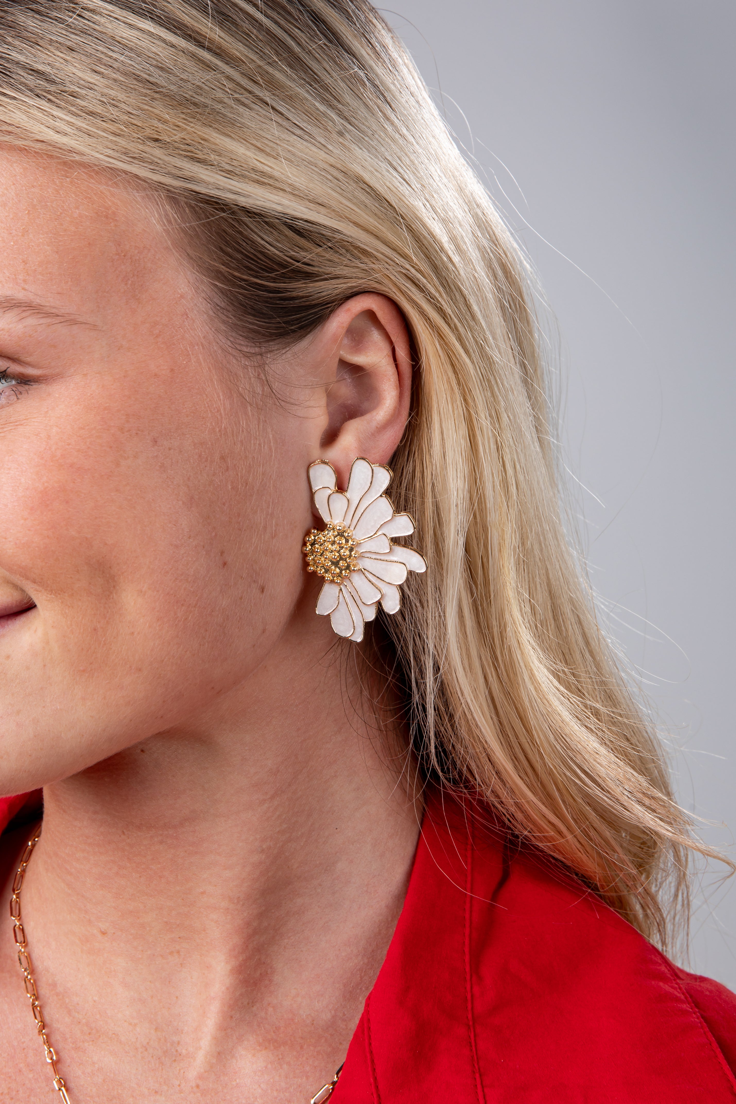 Close-up of a woman wearing a floral earring with a red top against a neutral background