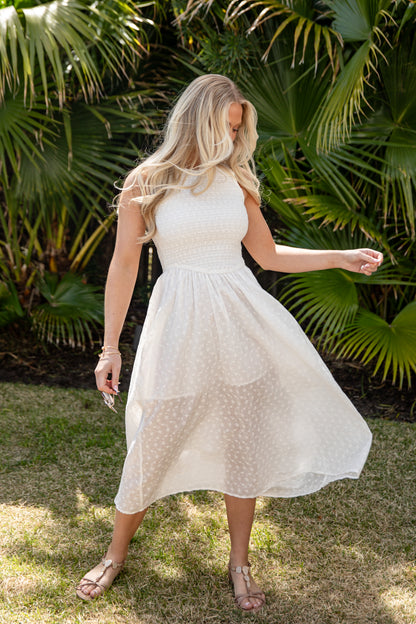 Woman in a white dress standing outdoors with green foliage in the background