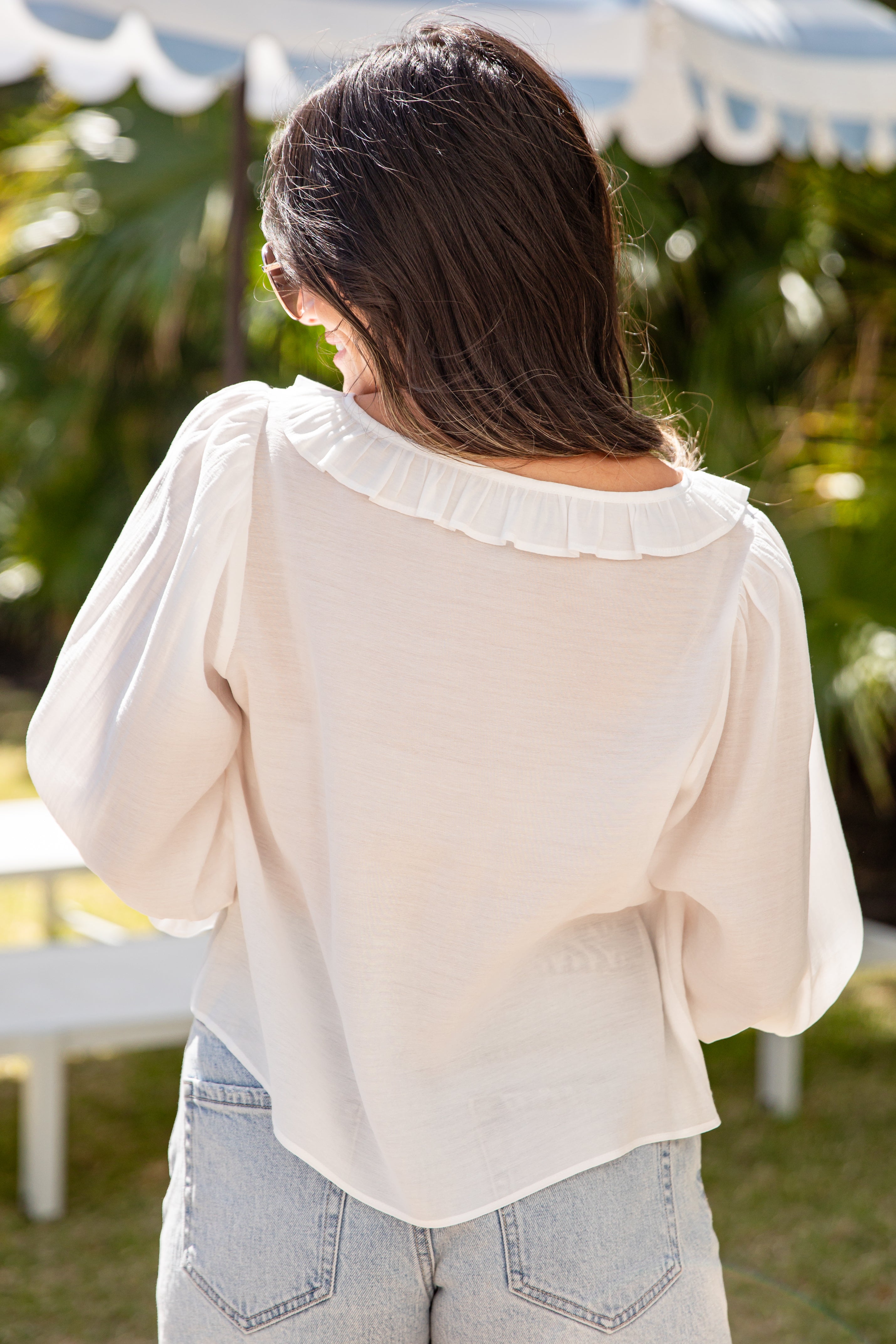 Woman wearing a light-colored blouse with ruffled collar in an outdoor setting