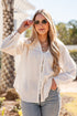 Woman wearing a white blouse and sunglasses outdoors with trees and a building in the background