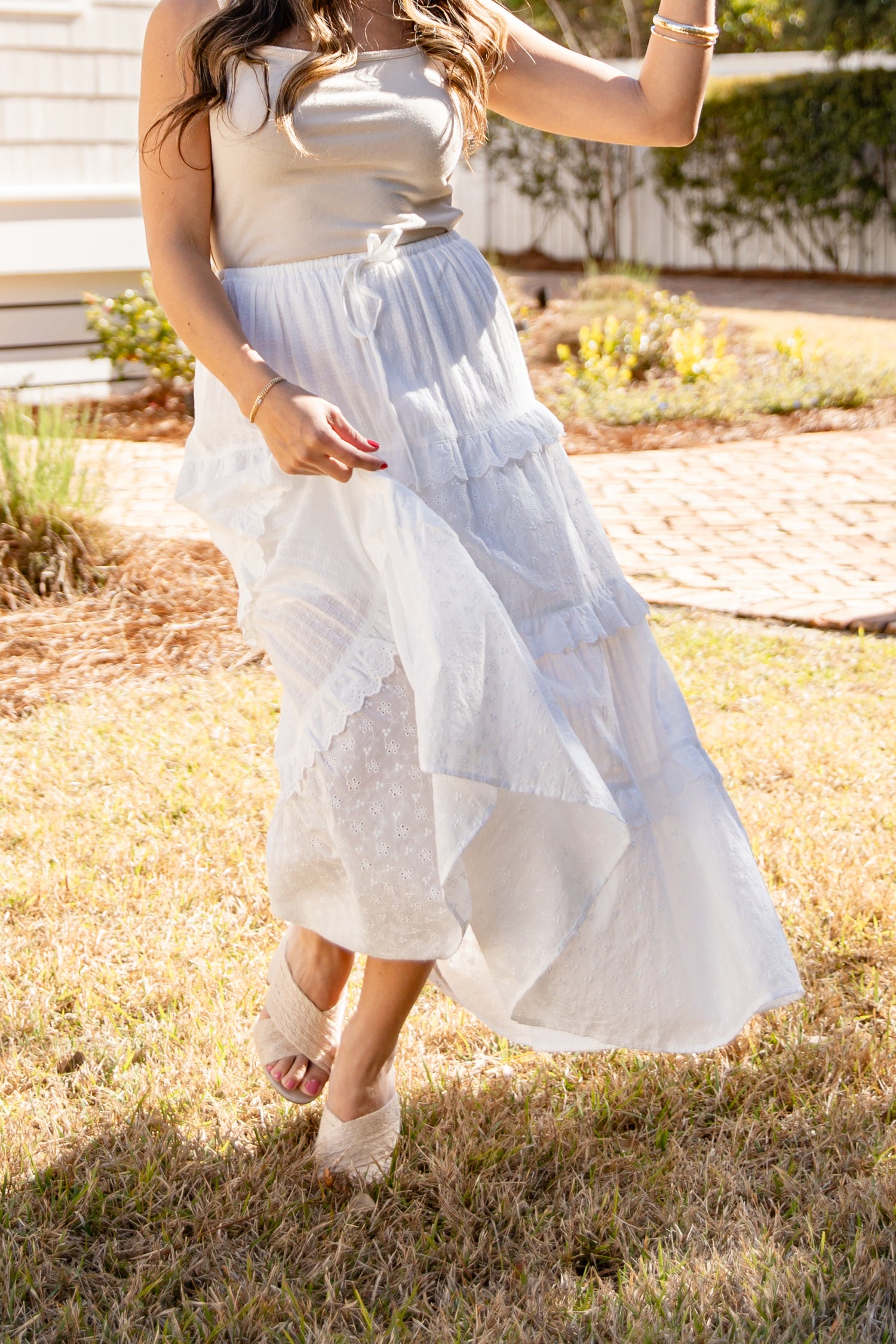 Woman wearing a beige top and white lace skirt standing outdoors on grass.