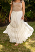 Woman wearing a beige top and white ruffled skirt standing outdoors on grass.