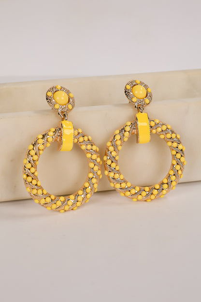 Yellow hoop earrings with intricate designs on a beige surface