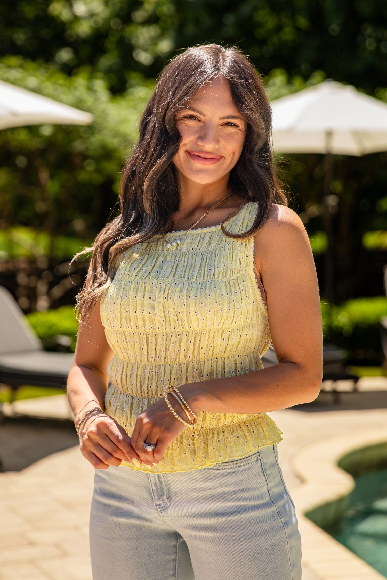 Woman standing outdoors with greenery and a pool in the background