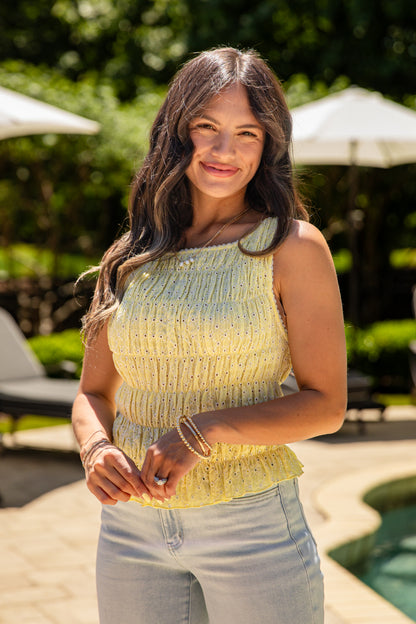 Woman standing outdoors with greenery and a pool in the background