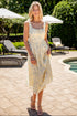 Woman in a floral dress standing by a poolside with lounge chairs and umbrellas in the background.