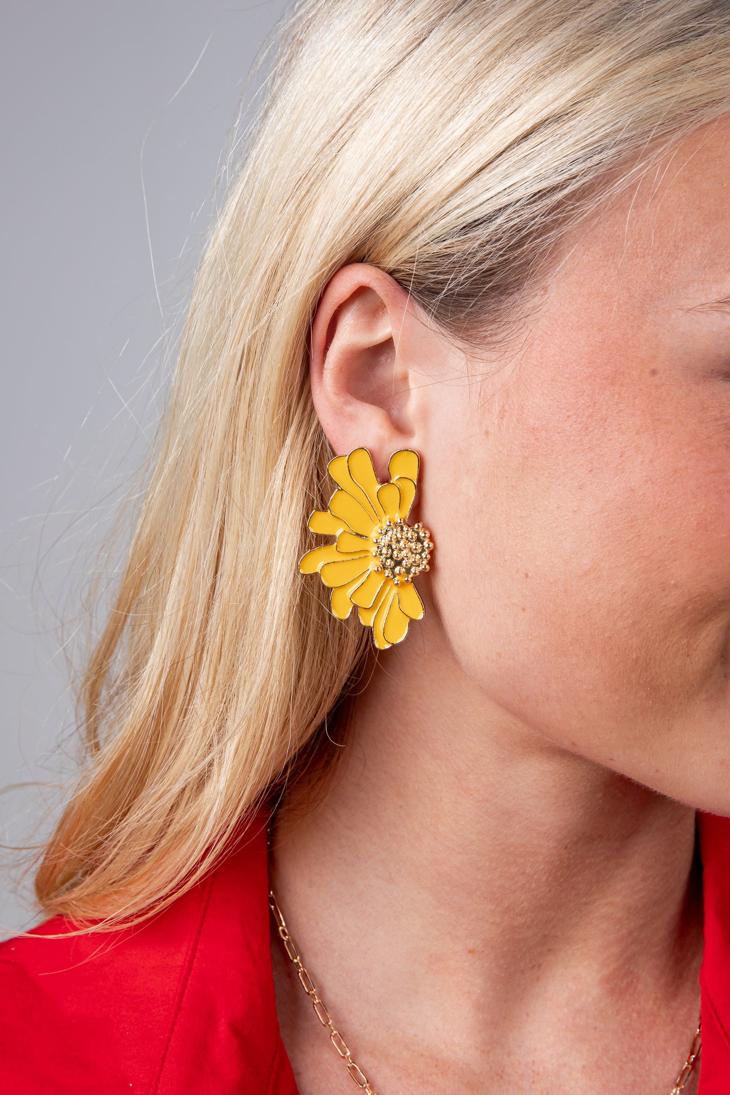 Close-up of a person wearing a yellow floral earring with a red top and gray background